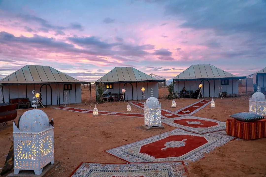 Interior of a Moroccan desert camp tent with rugs, a made bed and a lantern