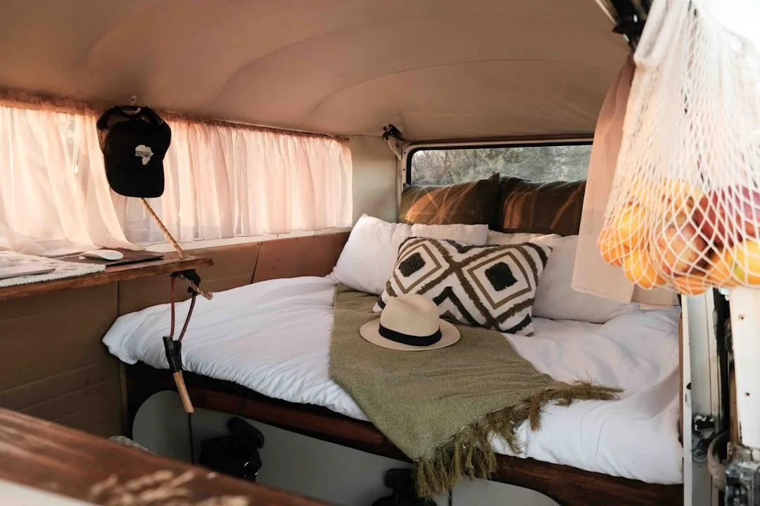Compact interior of an Airstream trailer showing a made bed beneath curved rear windows