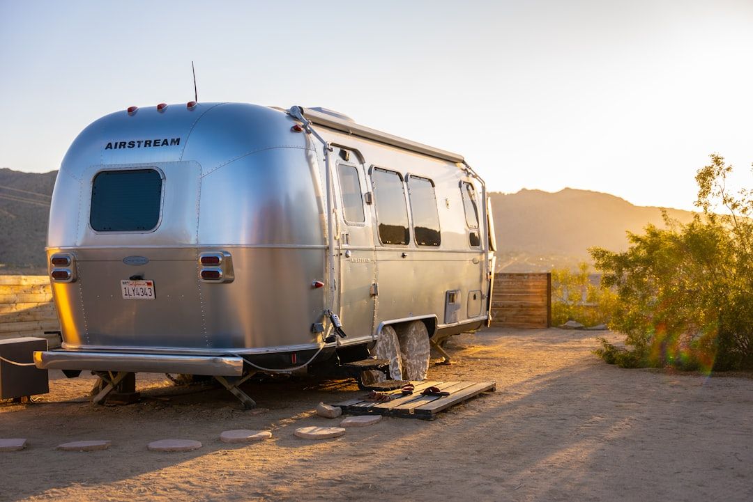 Silver Airstream trailer parked among tall trees with a wooden deck and fire pit